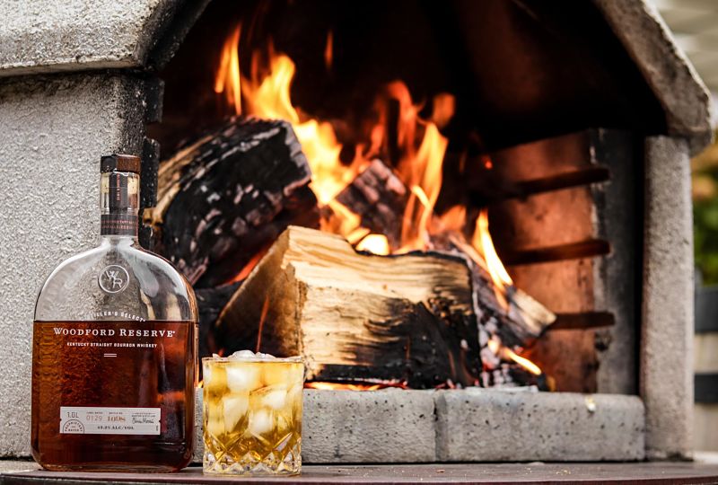 Madera quemándose en una barbacoa al fondo, delante de ella una botella de Woodford Reserve, tienda de bebidas en Salamanca